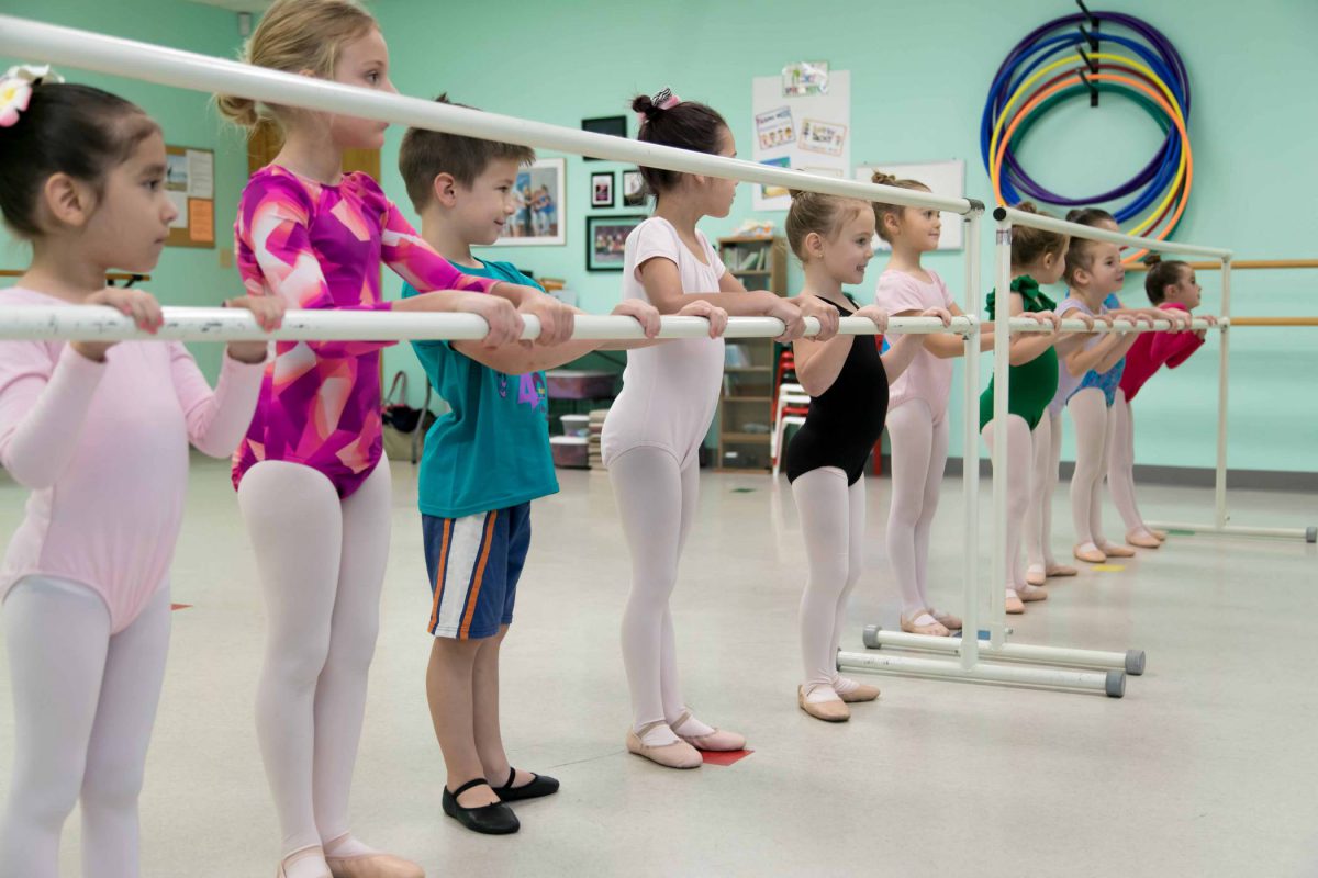 Group of young children in leotards and dance attire standing at the barre for ballet class