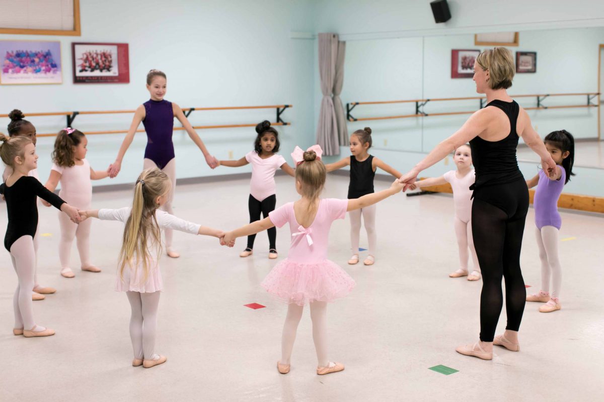 10 young female dance students standing in a circle in the studio with their teacher before starting preschool dance class