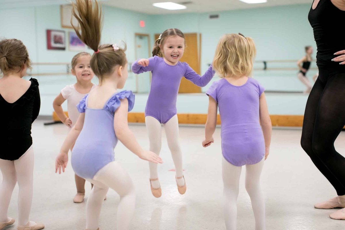 five female children in dance leotards, tights, and ballet slippers jumping and moving in preschool dance class