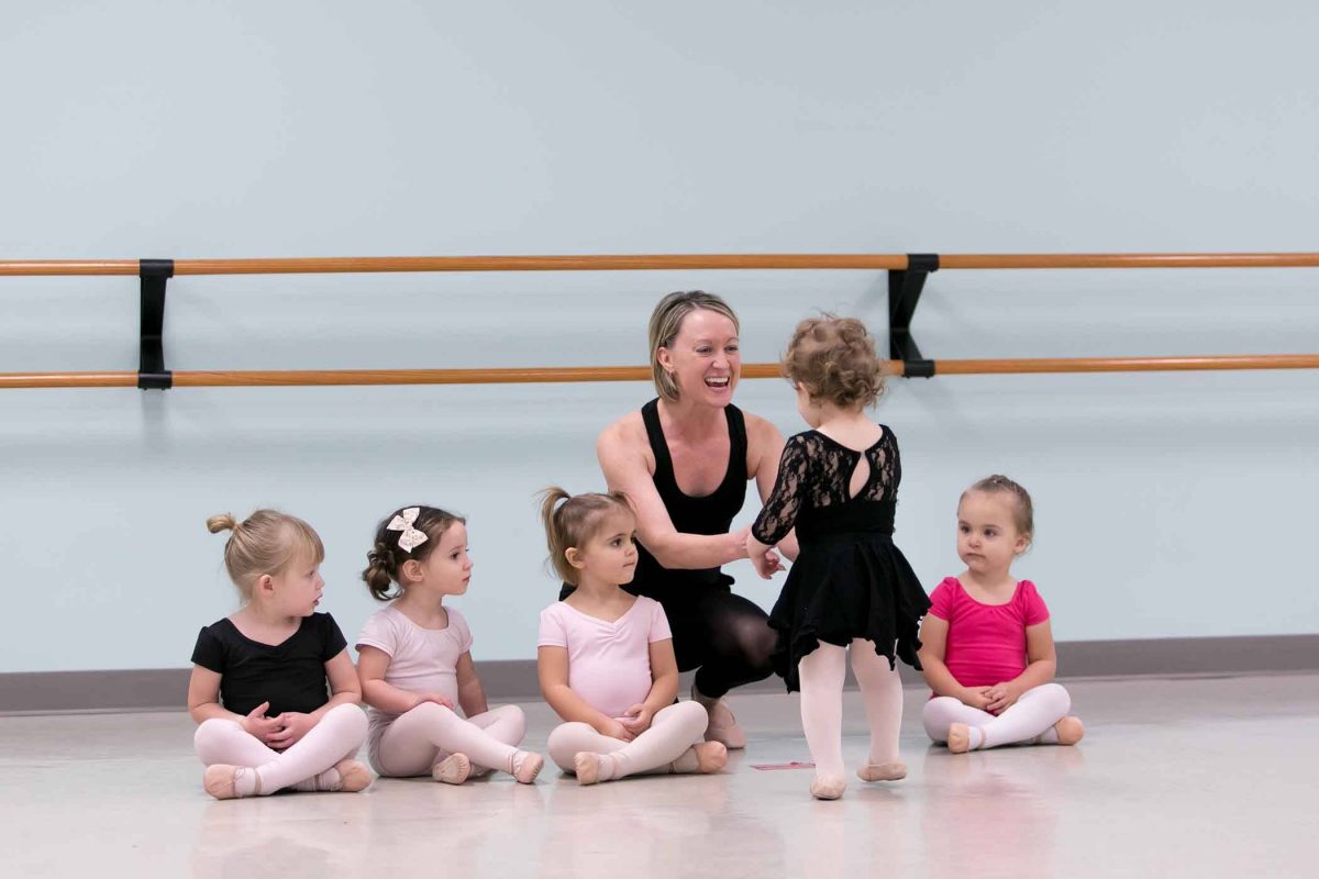 5 toddlers sitting and talking to their teacher in a ballet studio before preschool dance class